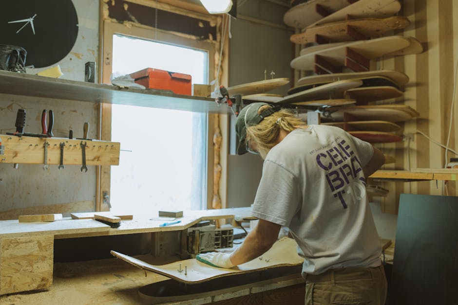 An artisan attentively customizes a skateboard deck in a well-equipped workshop.